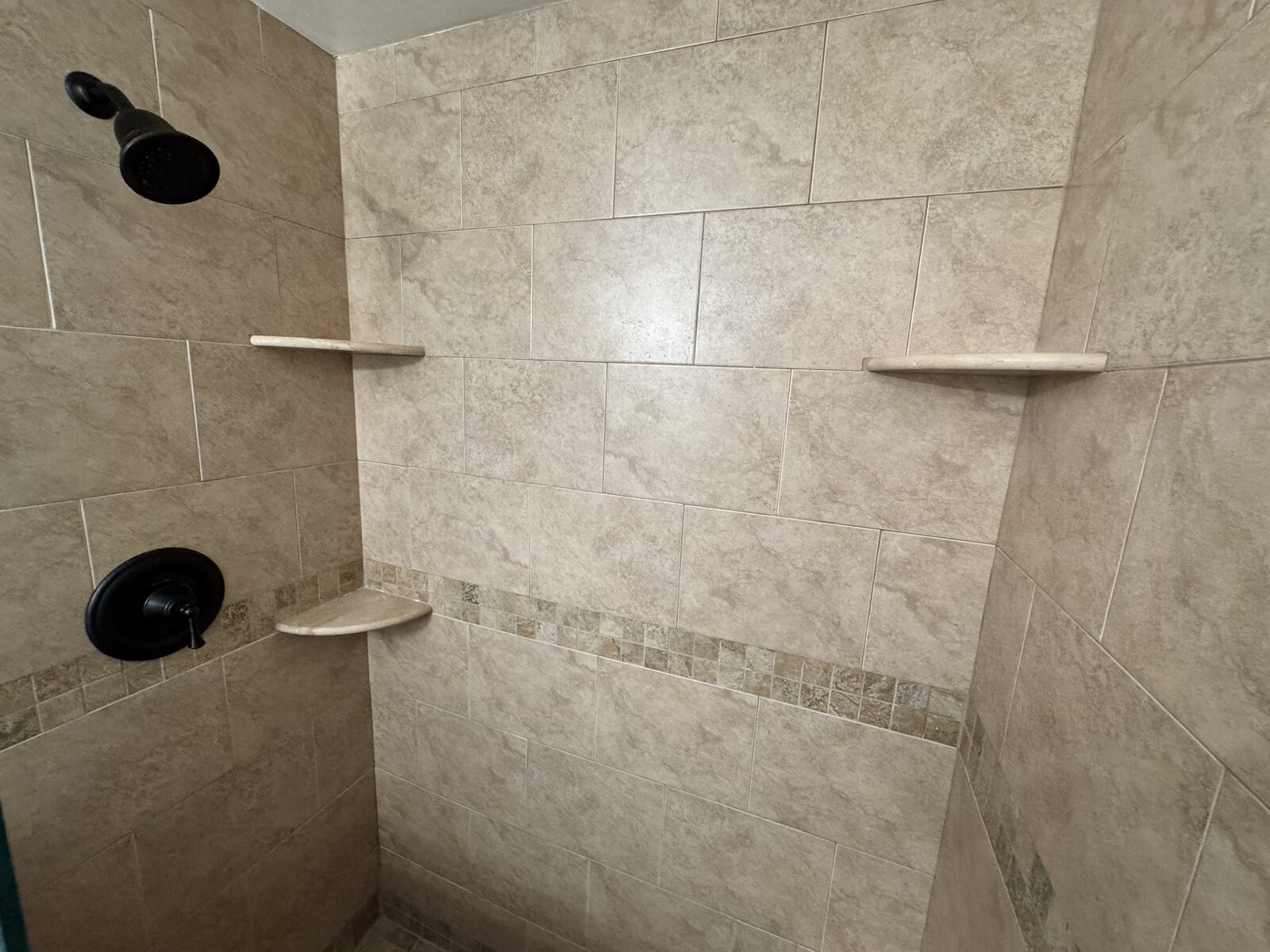 Tiled walk-in shower with corner shelves and matte black fixtures